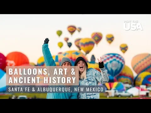 Twee lachende reizigers poseren voor kleurrijke luchtballonnen met de tekst Balloons Art and Ancient History Santa Fe and Albuquerque New Mexico