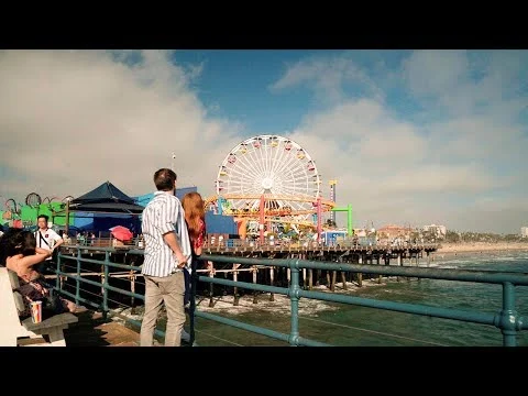 Bezoekers kijken vanaf de pier naar het kleurrijke reuzenrad en de attracties van Santa Monica Pier