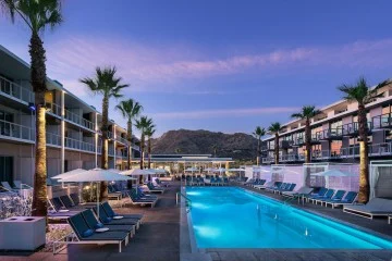 Verlicht zwembad tussen palmbomen bij een resort met ligstoelen en op de achtergrond een opvallende bergtop