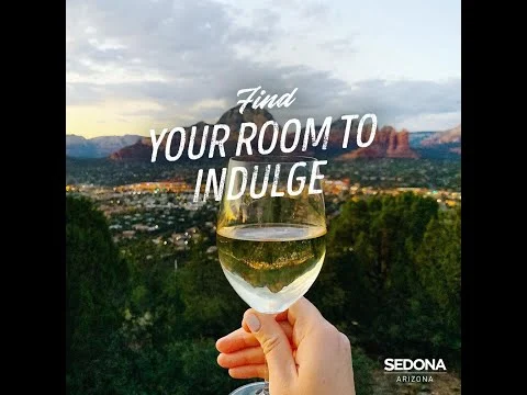 Promotievideo van Sedona met een hand die een glas witte wijn omhoog houdt tegen de skyline en rode rotsen bij zonsondergang