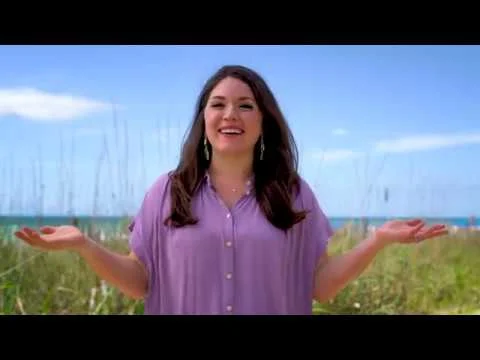 Vrouw met paarse blouse staat glimlachend tussen het strandgras op de duinen bij een strand in South Carolina