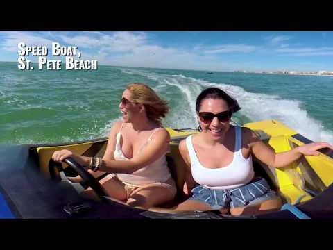 Twee lachende vrouwen varen in een gele speedboot over zee met de skyline van St. Pete Beach op de achtergrond