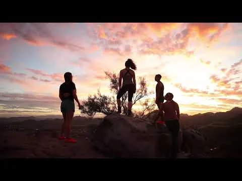 Silhouetten van vier wandelaars op een rotsformatie tegen een dramatische roze en oranje avondlucht bij Tucson