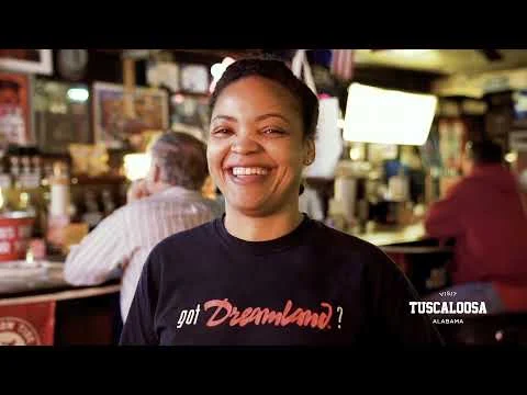 Lachende serveerster met dreamland-shirt staat achter de bar in een gezellig restaurant in Tuscaloosa, Alabama