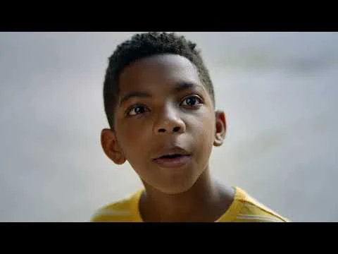Close-up portret van een jongen in een geel shirt die met open mond nieuwsgierig opzij kijkt, mogelijk in Tuskegee