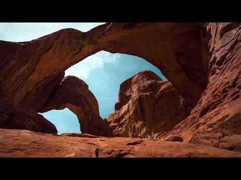 Videothumbnail met een uitzicht door een grote zandstenen rotsboog naar de blauwe lucht en omliggende rotsformaties in Arches National Park
