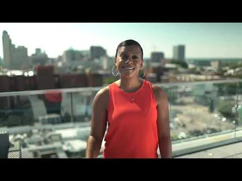 Lachende vrouw in oranje top staat op een dakterras met uitzicht op de skyline van een stad in Virginia