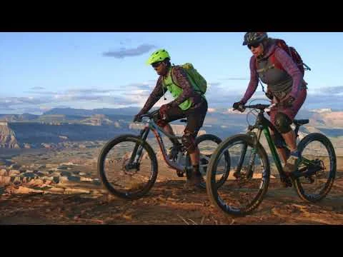 Twee mountainbikers staan met hun fietsen op een rotsachtig plateau met uitzicht over de canyons van Zion National Park