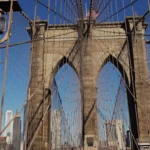 Close-up van de gotische stenen boogpijler van de Brooklyn Bridge met kabels en de skyline van Manhattan op de achtergrond