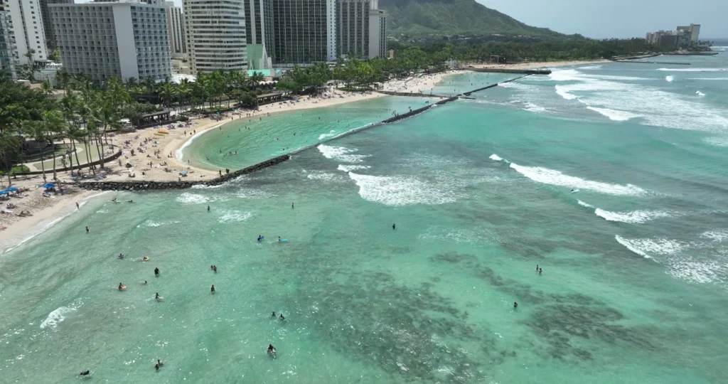Luchtfoto van hotels en palmbomen langs het witte strand van Waikiki Beach met zwemmers in turquoise water en de Diamond Head op de achtergrond