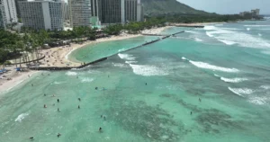 Luchtfoto van hotels en palmbomen langs het witte strand van Waikiki Beach met zwemmers in turquoise water en de Diamond Head op de achtergrond