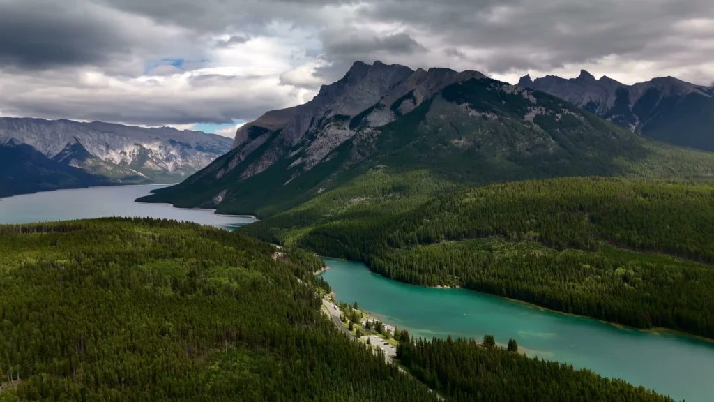 Luchtfoto van een turquoise meer omringd door dennenbossen en bergtoppen in de Canadese Rockies onder een bewolkte lucht