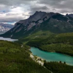 Luchtfoto van een turquoise meer omringd door dennenbossen en bergtoppen in de Canadese Rockies onder een bewolkte lucht