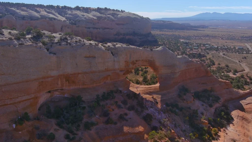 Grote natuurlijke boog van rode zandsteen torent boven een uitgestrekte canyon met struiken en verre bergen