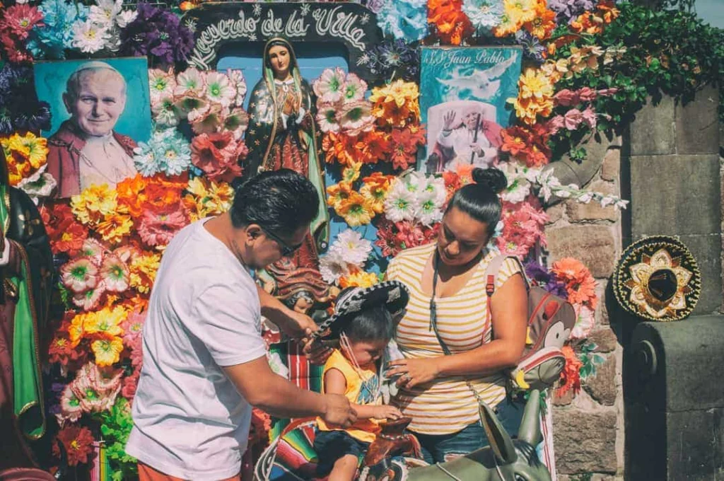 Ouders zetten een sombrero op bij hun kind voor een altaar versierd met bloemen tijdens een familiereis door Yucatán