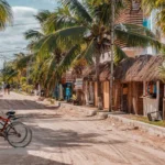 Zandweg met palmbomen en rieten daken in een rustig kustdorp in Yucatán, met een fiets op de voorgrond
