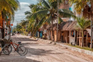 Zandweg met palmbomen en rieten daken in een rustig kustdorp in Yucatán, met een fiets op de voorgrond